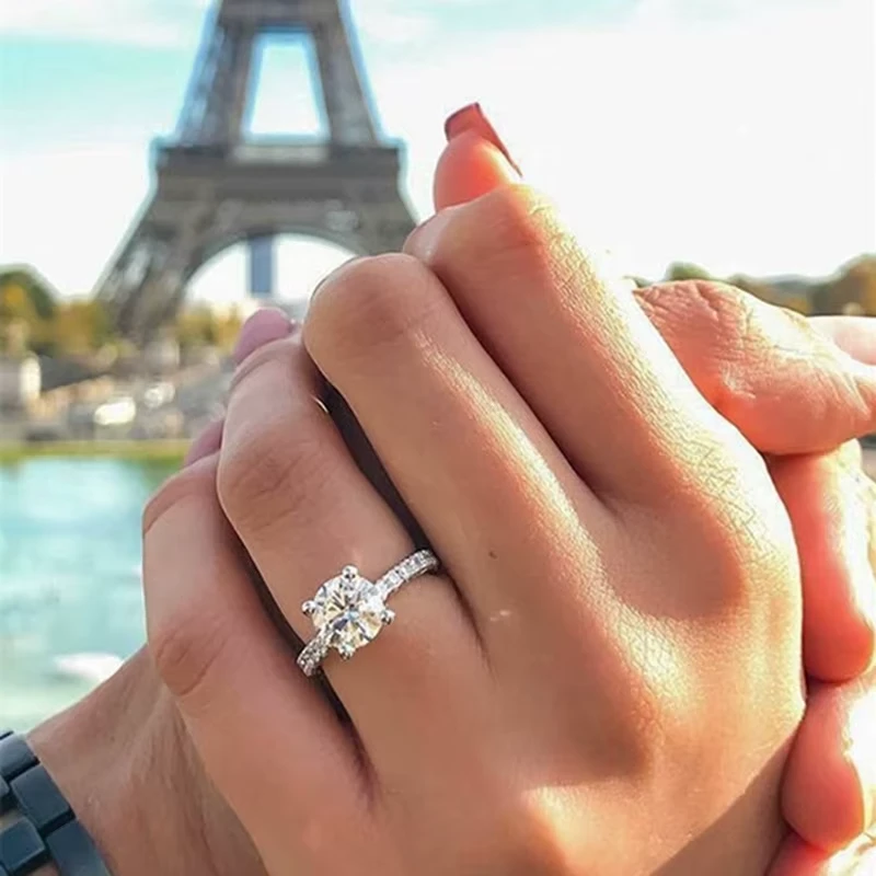 Une bague de fiançailles ornée d'un diamant étincelant tenue par un couple devant la Tour Eiffel, symbole romantique idéal pour une demande en mariage.