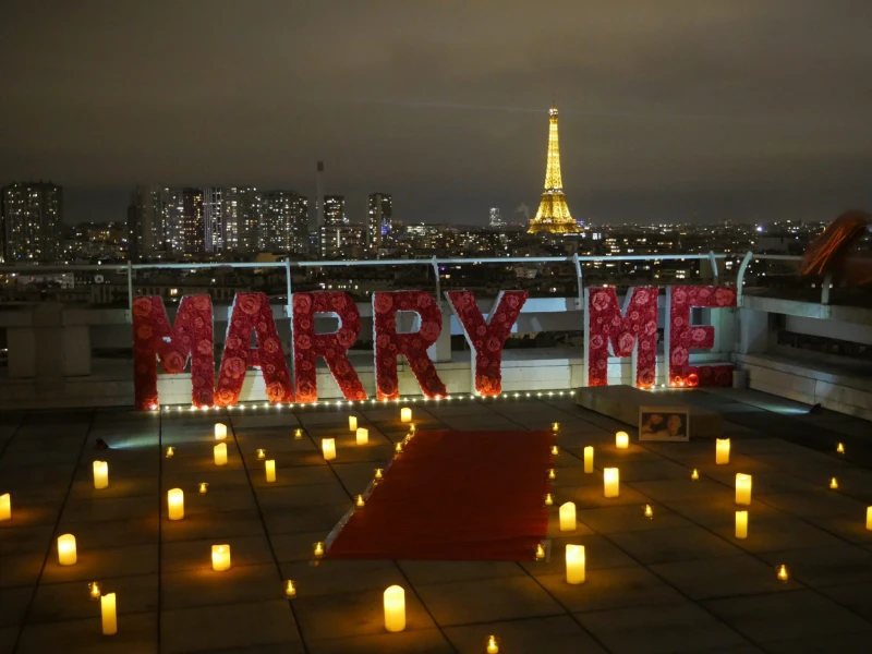 Une terrasse décorée avec des bougies et des lettres "Marry Me" face à la Tour Eiffel illuminée, créant une ambiance magique pour une demande en mariage.