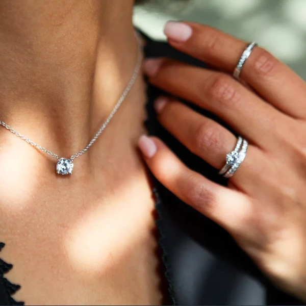 Gros plan d'une femme portant un collier en diamant et une bague de fiançailles étincelante, avec des alliances assorties, symbolisant l'élégance et le luxe.